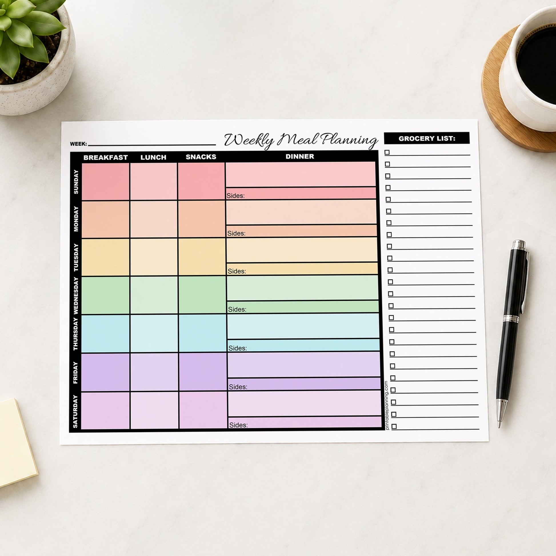A printed page of the Rainbow Weekly Meal Planner with Grocery List (printable page) displayed on a light marble surface, styled with a small potted succulent, a cup of coffee, and a black pen.