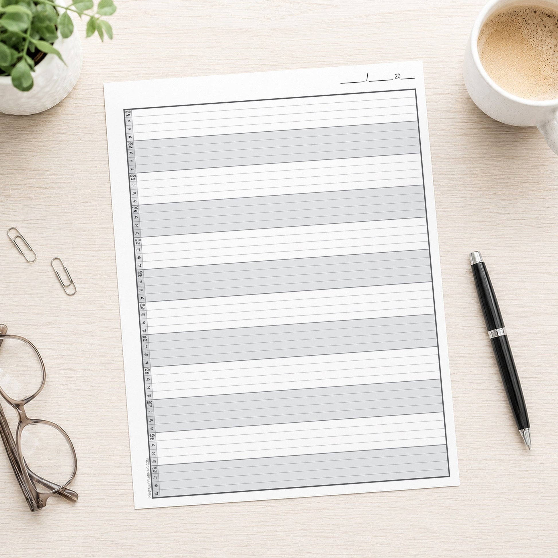 The printed Full-Width Schedule Sheet in 15-Minute Increments (printable front page) shown on a table with a plant, coffee, glasses, paperclips, and a pen.