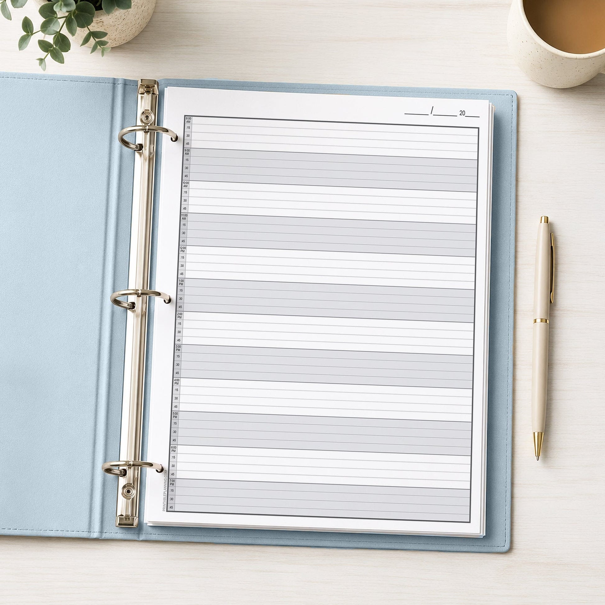 The printed Full-Width Schedule Sheet in 15-Minute Increments (printable front page) shown in a light blue binder on a desk with a plant, coffee, and a pen.