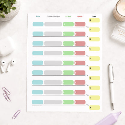 Simple Color-Coded Financial Transaction Register (printable page) shown on a light desk with earbuds, paperclips, highlighter, plant, and a pen.