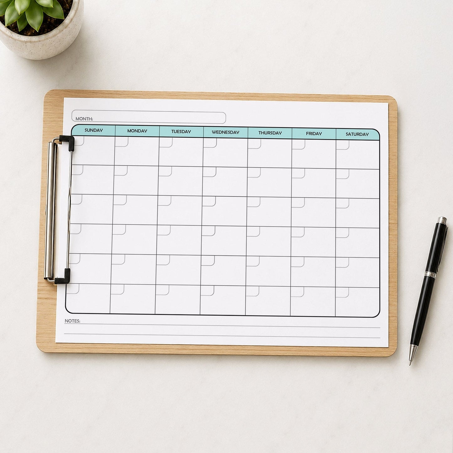 A printed Undated Monthly Calendar - Teal Full-Page Planner (printable) page shown on a wooden clipboard on a table with a plant and a pen.