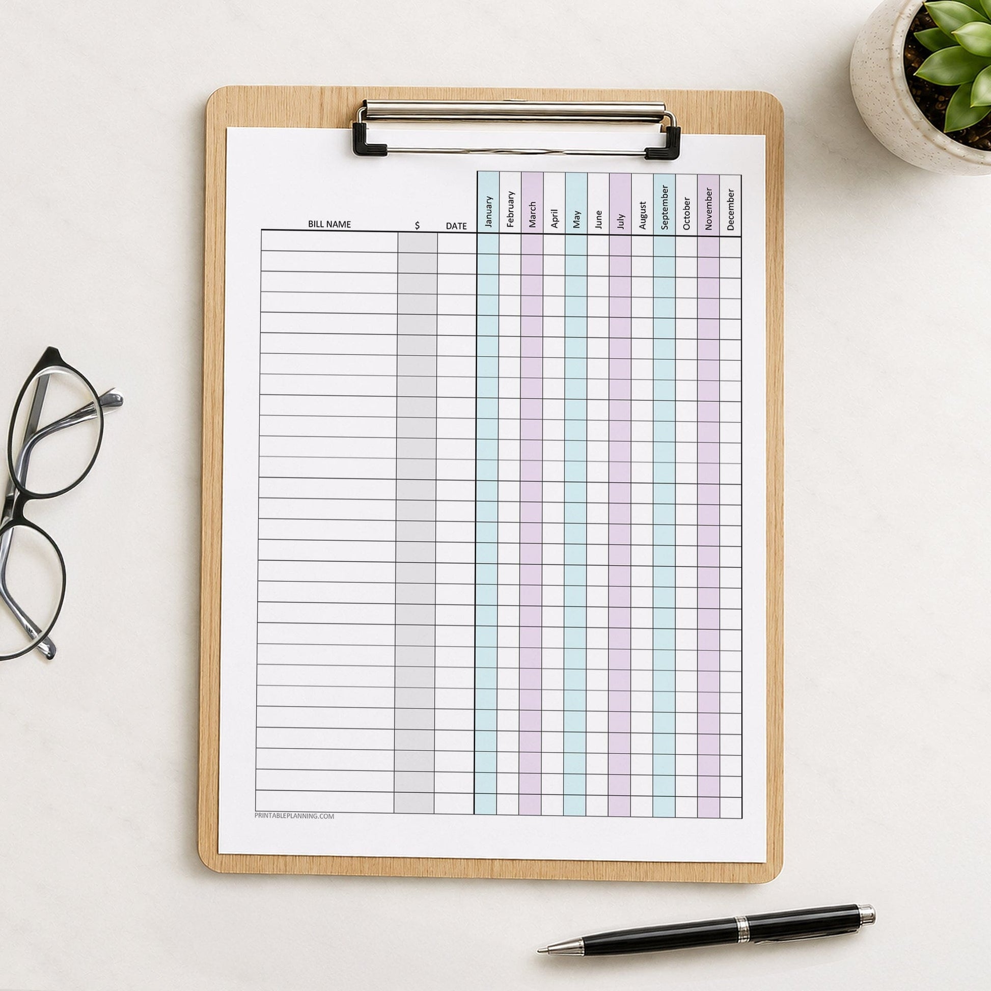 Turquoise Purple Yearly Bill Payment Tracker with Amount Column (printable page) shown on a wooden clipboard on a desk with glasses, a plant, and a pen.