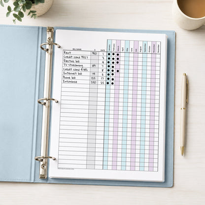The printed Turquoise Purple Yearly Bill Payment Tracker with Amount Column (printable) page, with example writing, shown in a light blue binder on a desk with a plant, coffee, and a pen.