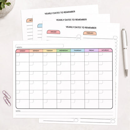 The 4 printed pages of the Undated Monthly Calendar & Important Dates Tracker Bundle shown on a desk with a plant, paperclips, and a pen.