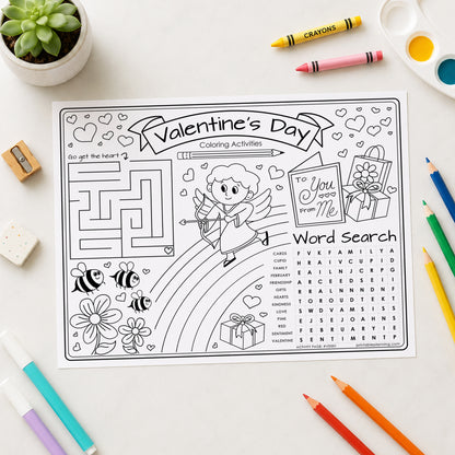 A Valentine's Day coloring activities sheet with black and white line art, surrounded by colorful crayons, colored pencils, a small potted succulent, and a paint palette on a white desk.