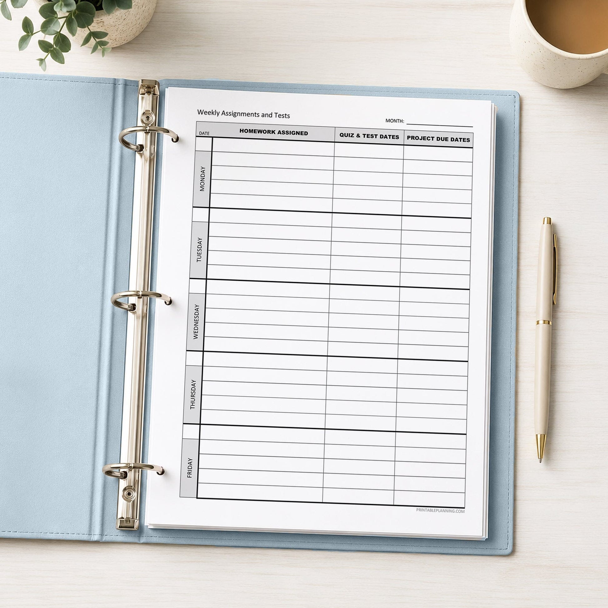 A printed Weekly Student Assignment Tracker for Homework, Tests & Projects (printable page) shown in a light blue binder on a desk with a plant, coffee, and a pen.