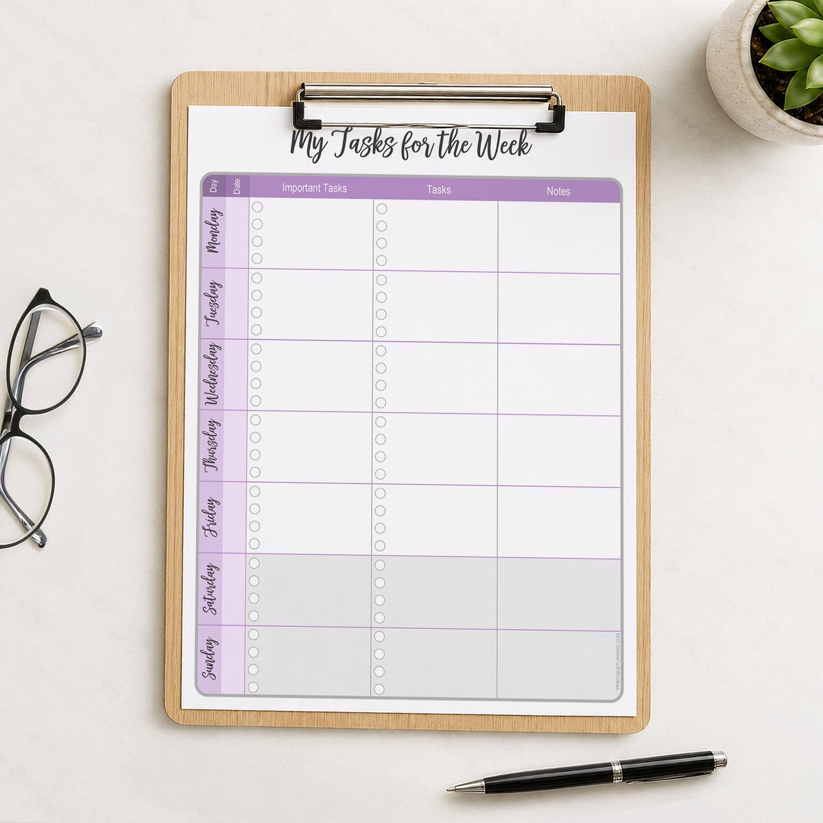 The printed Purple Weekly Task Planner with Priorities, Checklists & Notes (printable) page shown on a wooden clipboard on a table with  plant, glasses, and a pen.