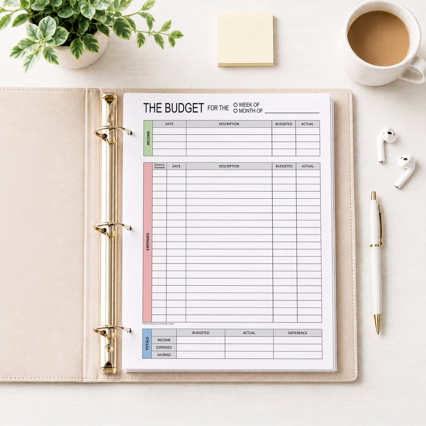 A printed page of the Weekly or Monthly Budget Worksheet - Printable Income and Expense Tracker shown in a beige binder on a desk with a plant, sticky notes, earbuds, coffee, and a pen.