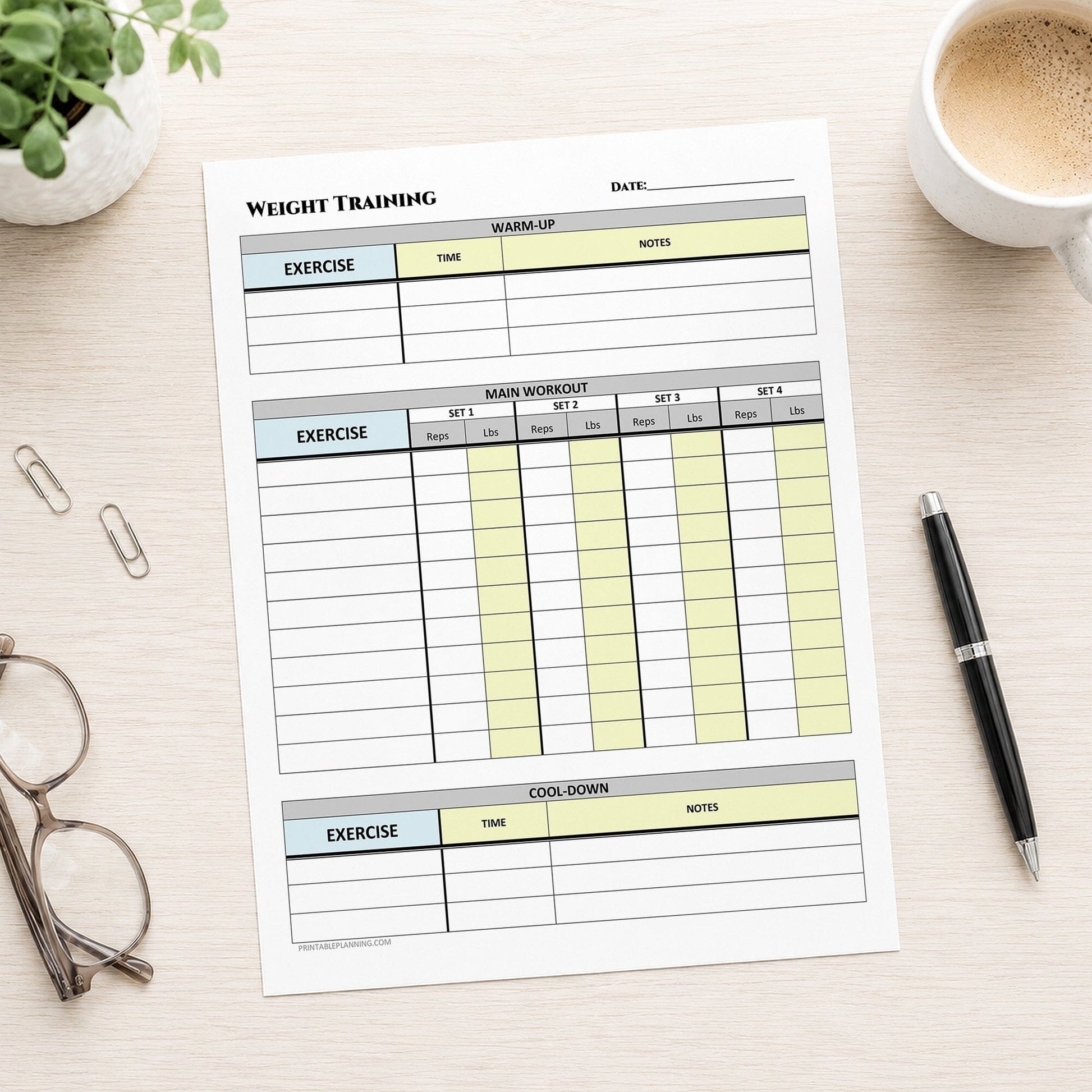 A printed Weight Training Workout Log with Warm-Up and Cool-Down (printable page) shown on a desk with a plant, coffee, glasses, paperclips, and a pen.